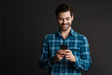 Joyful handsome brunette guy smiling and using cellphone