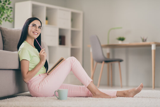 Profile Side View Of Pretty Cheery Creative Long-haired Girl Sitting On Carpet Writing Exercise Creating Solution At Light Interior Room