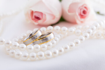 Modern wedding rings with pearl necklace wih pink roses in the background