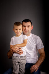 Portrait of happy father and son in white t-shirts on gray background. Dad hugs his son.