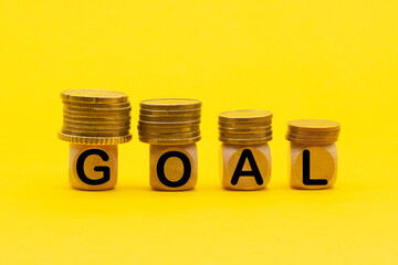wooden cubes with GOAL word with coins on top on a yellow background . Business success goal concept.