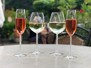 Four glasses with wine. Two glasses of rose wine and white wine on table in outdoor restaurant in summer.