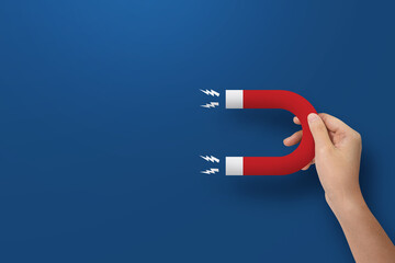 Close up of hand holding horseshoe magnet at blue background.