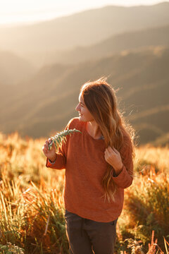 Carefree happy woman in sweater enjoying nature on grass meadow on top of mountain with sunrise. Beauty girl outdoor with sunbeams. Freedom concept
