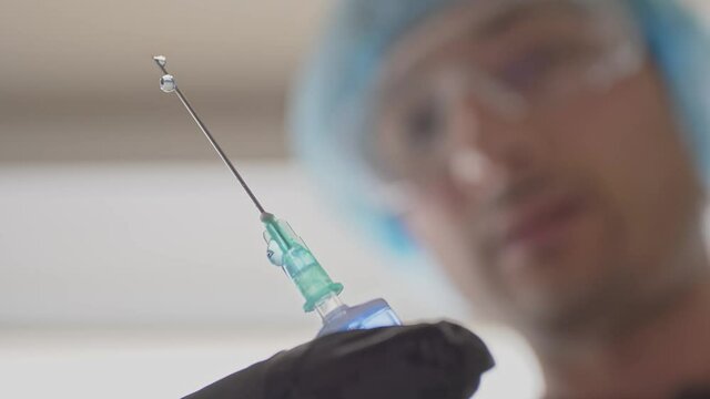 Blurred image of a medic with a syringe in his hand. A researcher pushes air bubbles out of the serum before use Syringe needle with drops. Vaccination concept
