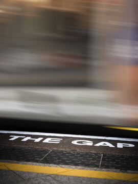 Mind the gap white writing sign painted on train station platform with engine and carriages in motion passing through by high speed blurred by fast travel underground stand behind yellow line