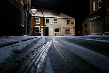 Dark icy road frozen highway high street junction winter salt spreading during severe weather. Dangerous conditions for driving give way carriageway tracks no gritters out at night - obrazy, fototapety, plakaty