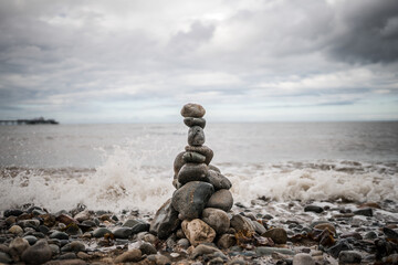 Pile of stones stacked up balancing sea shore ocean lapping up pebbles tower grey granite with...