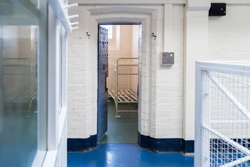 Looking into prison cell block victorian British English jail house with bed in room lock up high security room derelict old new category A B C in custody with bars door open confined escaping - obrazy, fototapety, plakaty