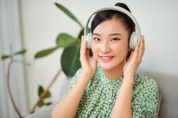 Fototapeta premium Woman listening music in headphones while sitting on sofa in room