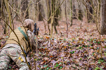 Beautiful girl in military uniform with an airsoft gun lying on the ground in the forest
