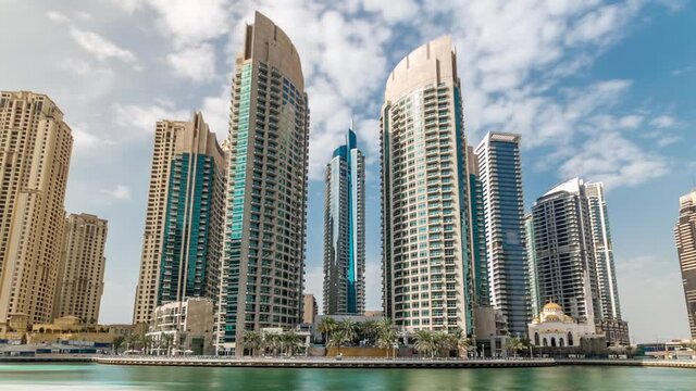 Dubai Marina modern towers with floating yachts and boats from promenade timelapse, United Arab Emirates. Tallest skyscrapers skyline. Blue cloudy sky