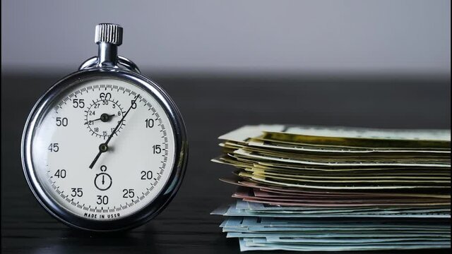 The stopwatch is lying on the table, and a hand is rapidly counting out dollar bills next to it, and the hand is ticking. The concept of sales, discounts and investments in stocks and businesses. time