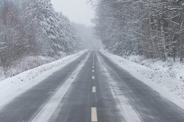 Asfaltowa droga prowadząca przez las pokryty grubą warstwą  śniegu.