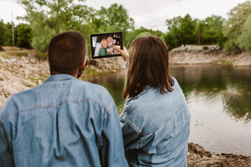  Couple in love camping.Couple sit near the lake and using digital tablet for video call.