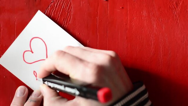 A woman's hand writes a heart and the word "love"on a sticker with a red marker.