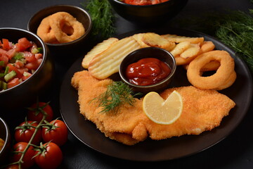 Meat schnitzel and fried potatoes with onion rings deep fried, vegetable salad