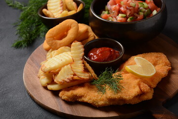Meat schnitzel and fried potatoes with onion rings deep fried, vegetable salad