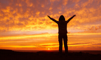 Fototapeta premium Woman hiker with hands up arms during sunset. Silhouette of an unrecognizable female.