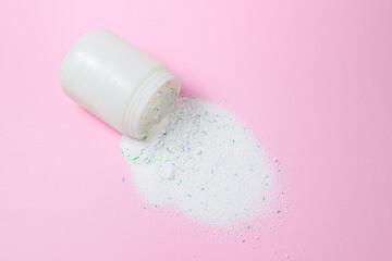 Laundry detergent on a pink background. Washing powder spilled out of the measuring cup. Household...