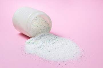 Laundry detergent on a pink background. Washing powder spilled out of the measuring cup. Household chemicals