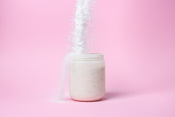 Laundry detergent on a pink background. The washing powder is poured into a measuring cup. Household chemicals