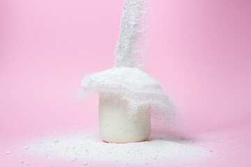 Laundry detergent on a pink background. The washing powder is poured into a measuring cup. Household chemicals