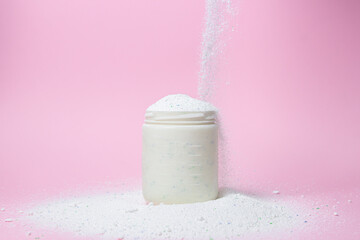 Laundry detergent on a pink background. The washing powder is poured into a measuring cup....
