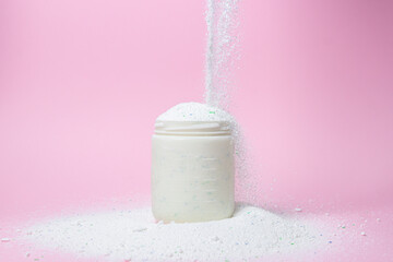 Laundry detergent on a pink background. The washing powder is poured into a measuring cup....