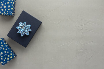 Fototapeta na wymiar Blue gift box and boxes in blue beautiful wrapper with stars and a bows on a gray concrete background, birthday or valentine concept, top view, copy space