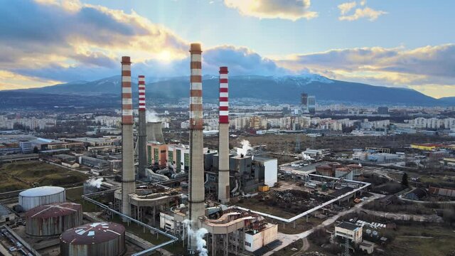Chimneys of thermal power plants. Aerial view of Industrial area, city and mountains. The sun setting behind the mountain. Dramatic clouds in the sky. Drone footage in 4k