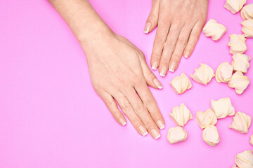 Beautiful Female Hands with French manicure and marshmallows over colorful pink paper background