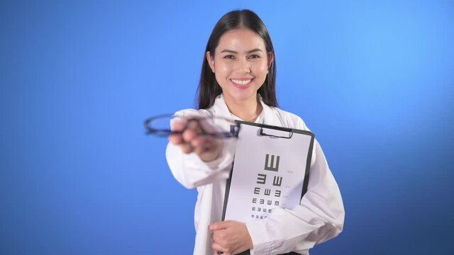 Young female ophthalmologist with glasses holding eye chart over blue background studio, healthcare concept