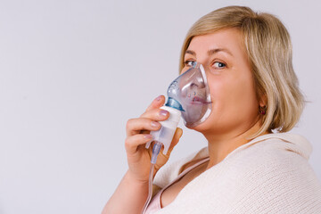 Senior woman using a nebulizer makes inhalation at home and looks at the camera. Empty space for advertising.