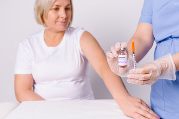 Senior woman and the hands of a nurse holding a syringe and a vaccine for covid 19. Fighting the spread of the virus on a white background.