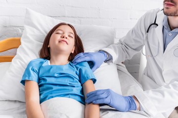 Obraz premium pediatrician examining diseased girl lying in bed with closed eyes