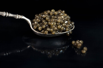 Black caviar delicate Russian beluga fish on a silver spoon . black background. Reflection in a...