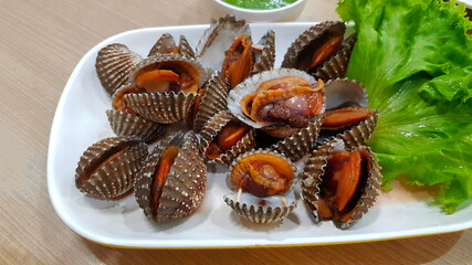 Fresh Scallop or cockle with green cabbage on white dish or plate and spicy sour sauce in Thai style on wooden table with copy space at seafood restaurant. Asian food and Delicious meal.