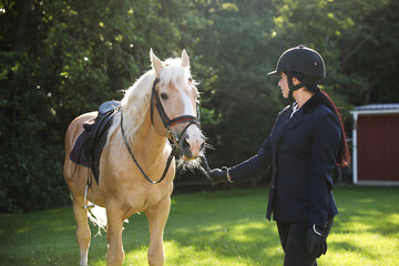 Obraz premium Young woman in horse riding suit and her beautiful pet outdoors on sunny day