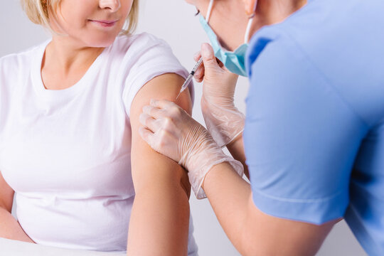 Enlarged Photo Where A Nurse Puts An Injection In The Shoulder Of A Senior Woman Against Covid 19. Vaccination Of The Elderly On A White Background.