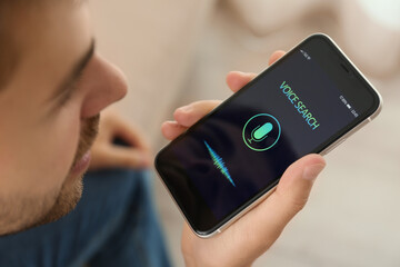 Young man using voice search on smartphone indoors, closeup