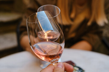 A glasses of rose wine in the hands of a girl and man who relaxing on restaurant terrace. Summer holiday. Celebrate and enjoy moment. Alcoholic drink tasting. Romantic evening aperitif