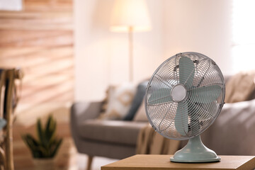 Modern electric fan on wooden table in living room. Space for text