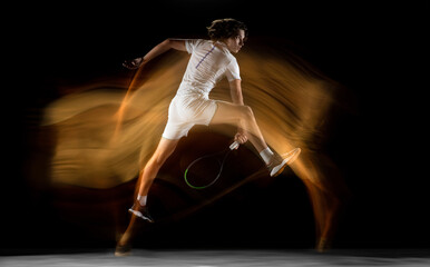 Flying. Young professional sportsman playing tennis isolated on black background in mixed light. Training, practicing in motion, action. Power and energy. Movement, ad, sport, healthy lifestyle