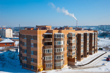 A five-storey residential building in winter and a chimney with smoke. 