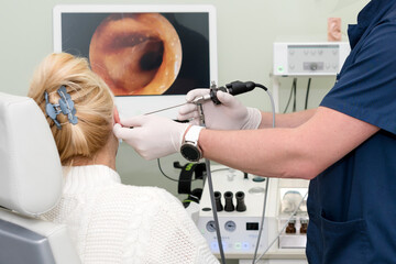 ENT doctor with tools wearing mask and gloves examines the patient's ear. Otolaryngologist doing...