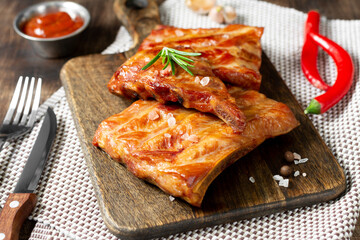 Cooked smoked pork ribs on a wooden serving board on a brown wooden table. Fried smoked pork ribs