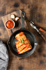 Boiled smoked pork ribs in a black cast-iron skillet on a brown wooden table. Fried pork ribs	