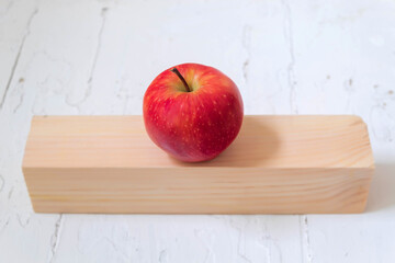 A fresh juicy apple of red color lies on a wooden stand on a light background