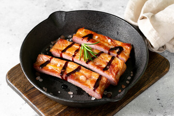  Boiled smoked pork ribs in a black cast-iron skillet on a light gray kitchen table. Fried pork ribs